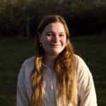 Tegwyn Hughes smiles and looks at the camera. She is white and has long blonde hair. She is wearing a white button-down shirt.