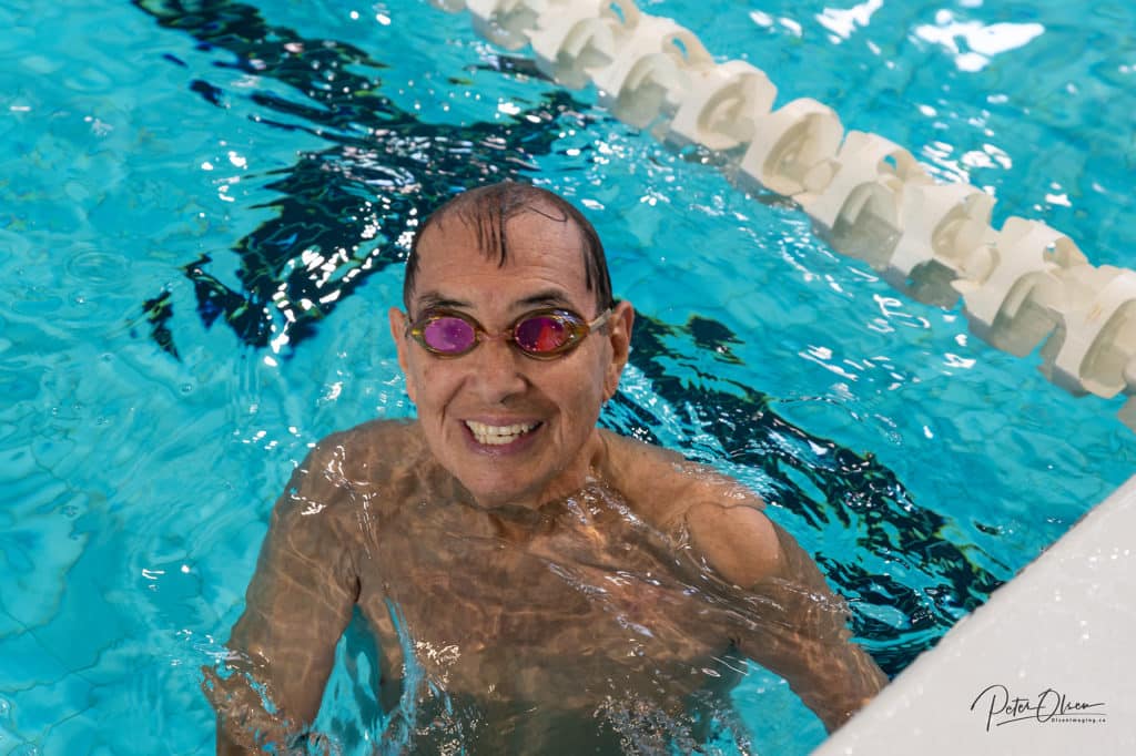 A person poses for the camera in a pool with goggles on, smiling.