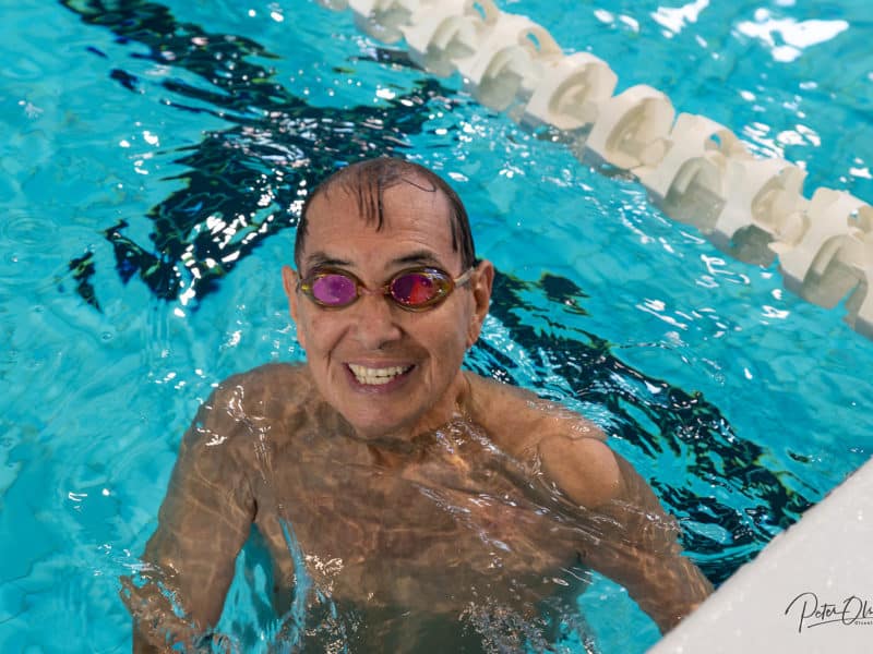 A person poses for the camera in a pool with goggles on, smiling.