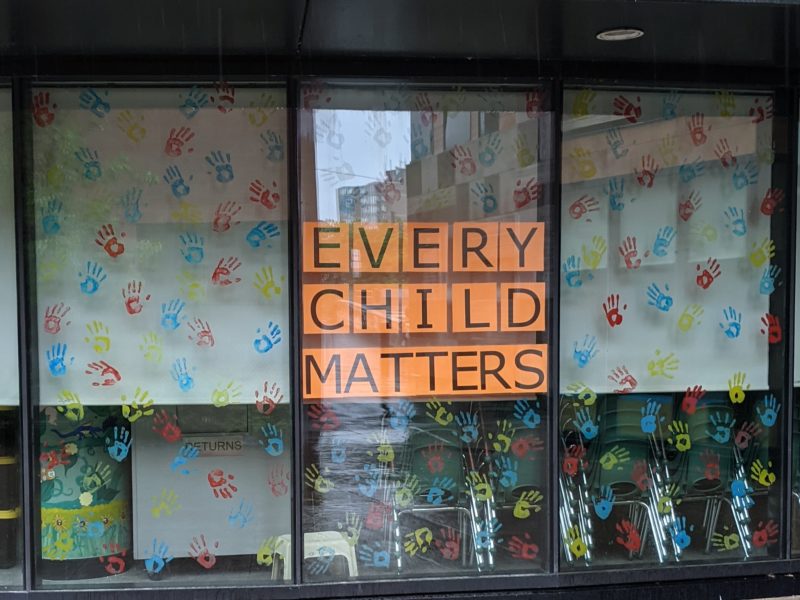 An orange poster hangs in the window of a school room and reads Every Child Matters.