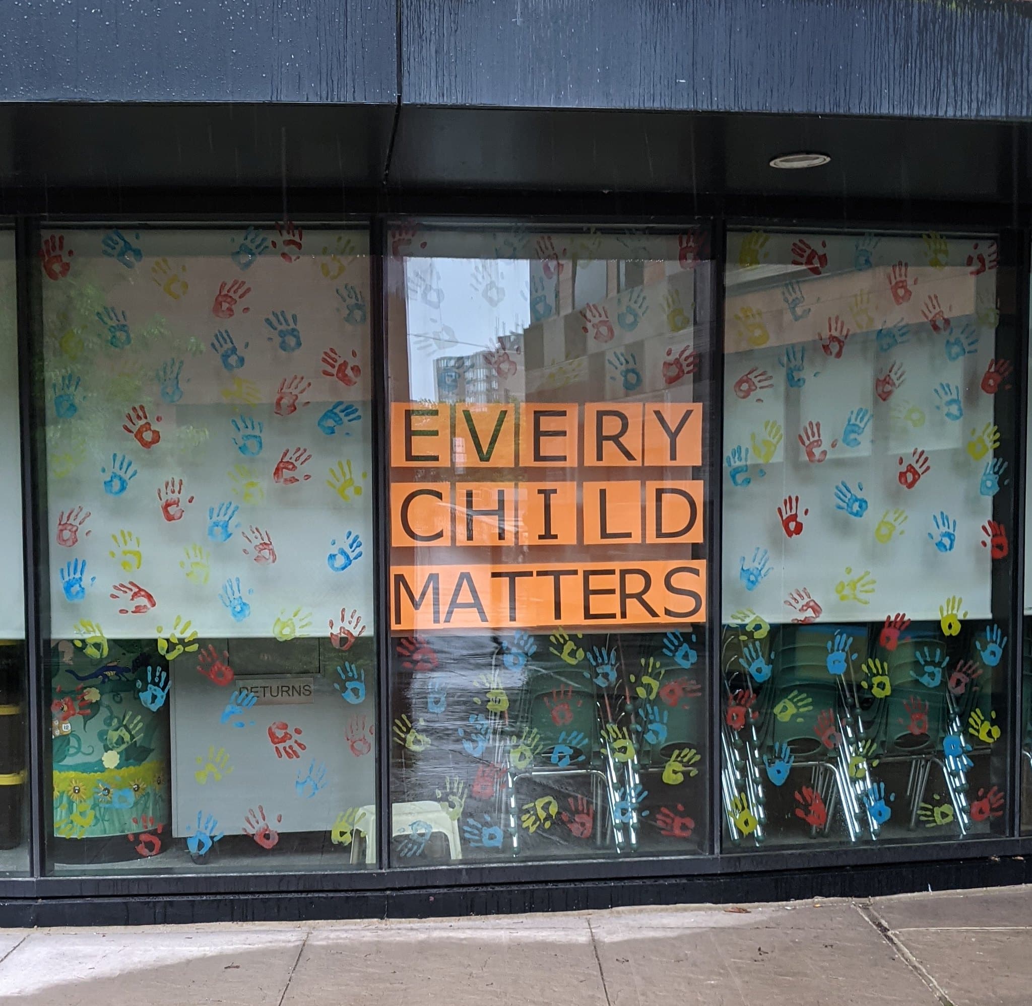 An orange poster hangs in the window of a school room and reads Every Child Matters.
