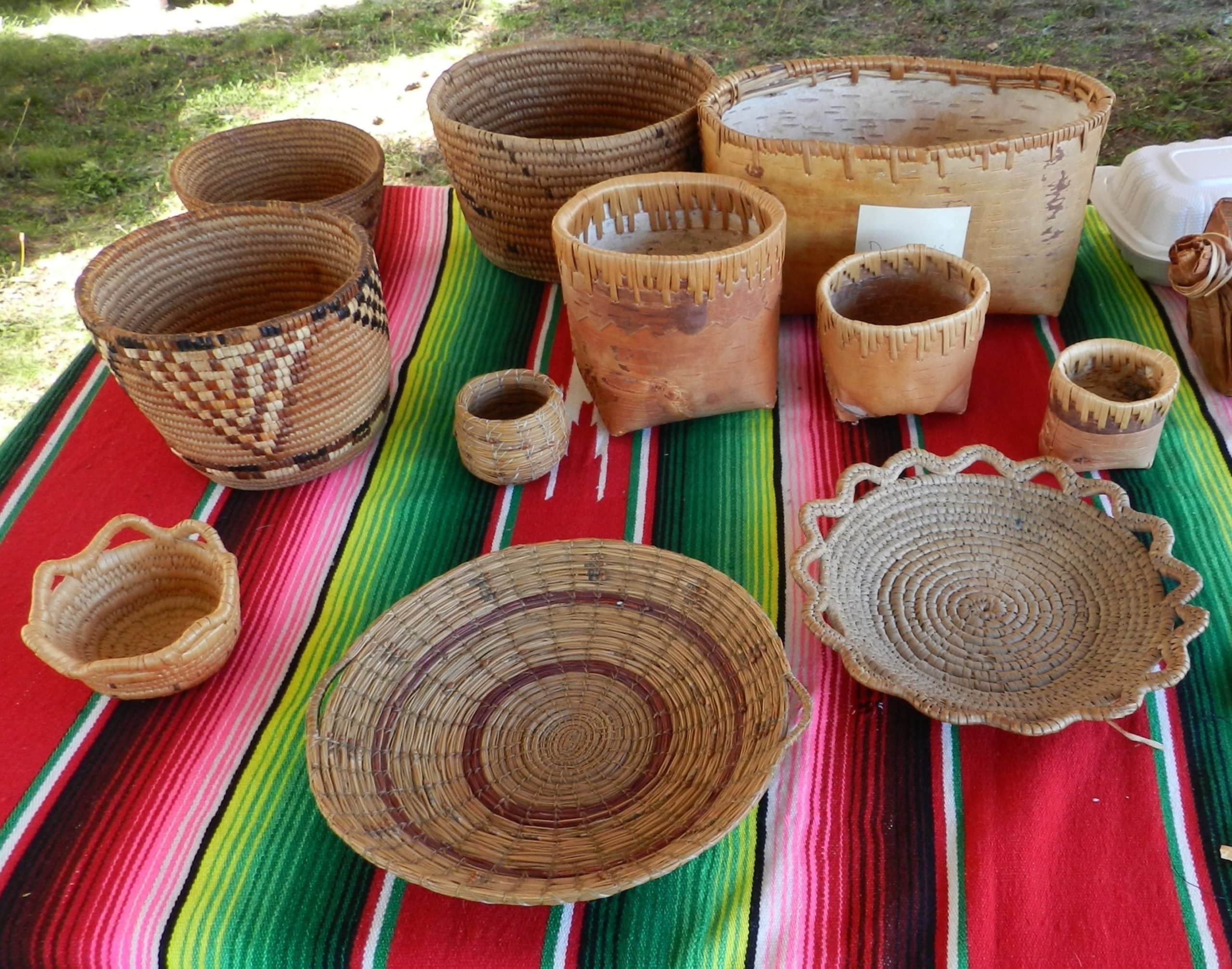 A selection of traditional Secwépemc baskets in different shapes and colours sits on a striped blanket.
