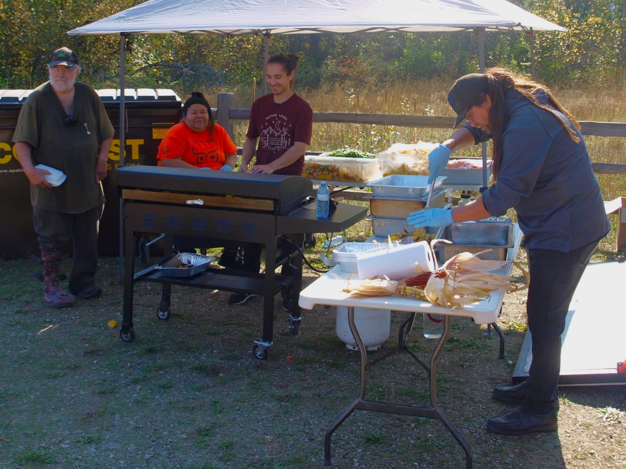A team of volunteers work together to prepare the feast. One prepares corn, while another works at the grill.