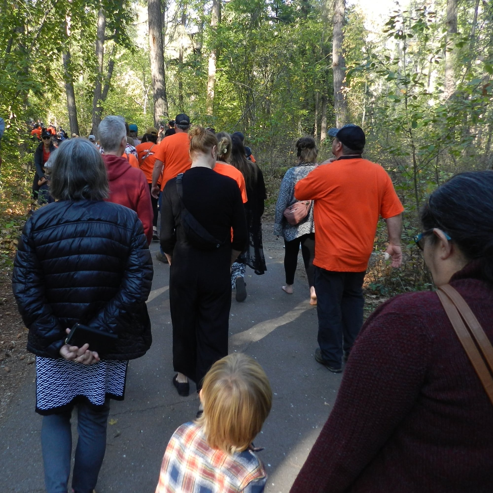 A group of attendees walks through a forested path, many wearing orange shirts to mark the National Day for Truth and Reconciliation. 