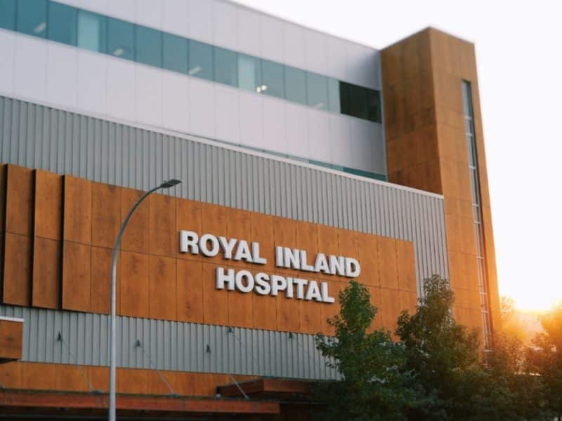 Royal Inland Hospital glows at sunset amid doctors shortage. International medical graduates could help stem shortage but the province continues to put up barriers. The hospital grows orange against a warm and sunlit background.