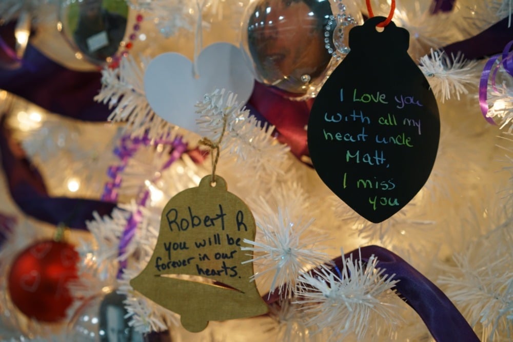 A close up of two paper ornaments hung on a white tree. One says "Robert R you will be forever in our hearts" while the other says "I love you with all my heart uncle Matt, I miss you."