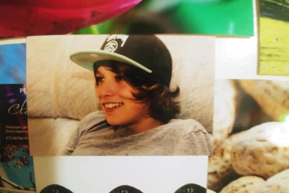 Printed photos are spread out, with one taking up most of the image. The photo portrays a young Jessie Simpson before his 2016 assault. In the photo, Simpson wears a baseball cap and grey t-shirt.