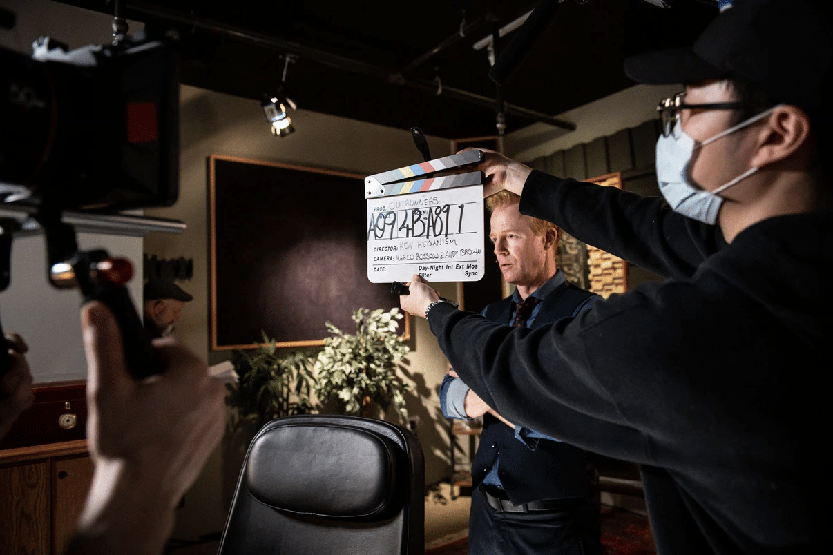 On the Outrunners film set, an actor prepares to act out a scene while a crew member holds a clapperboard in front of his face