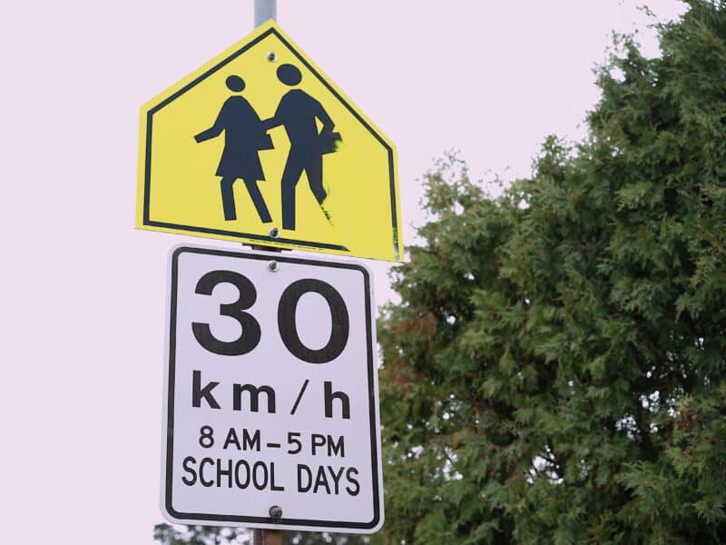 A school zone sign reads 30 km/ hr 8 AM - 5 PM SCHOOL DAYS as a safety precaution within a car-dependent culture