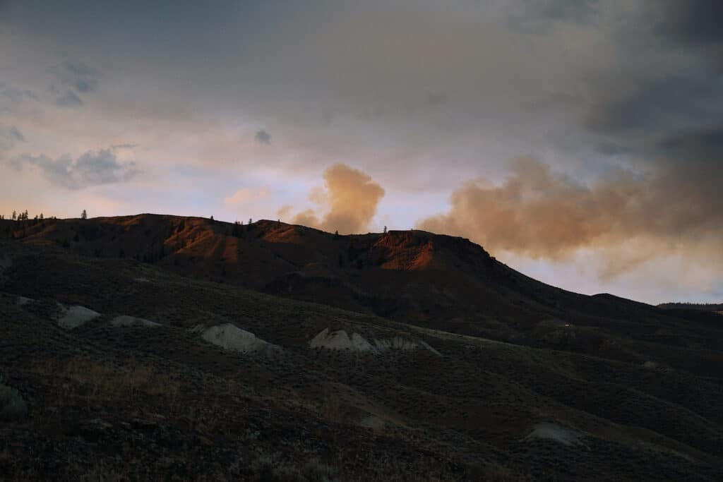 A smoke plume glows orange against blue skies at sunset in Kamloops near Tranquille Creek Park, Lac Du Bois Grasslands.