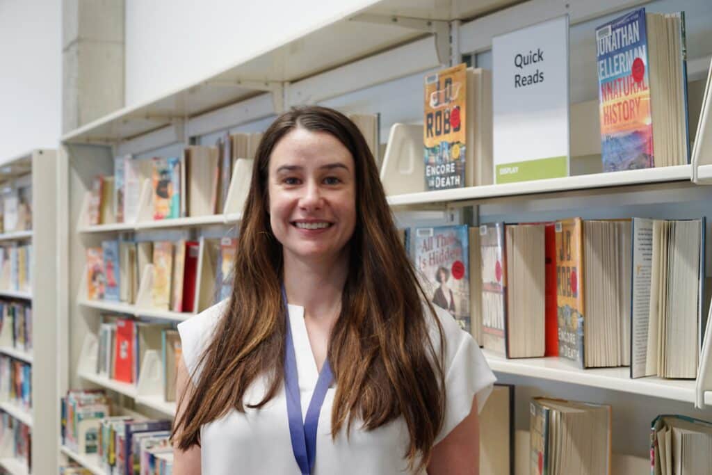 A woman with long brown hair smiles as she poses for a picture in front of a row of books at TNRL