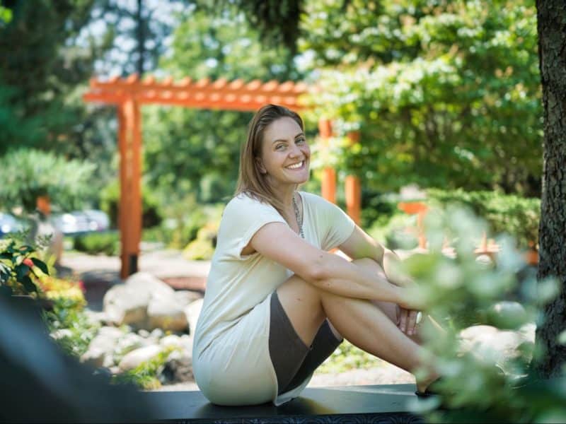 Stellar Feels Embodiment owner Vanessa Woulfe sits in a park smiling.