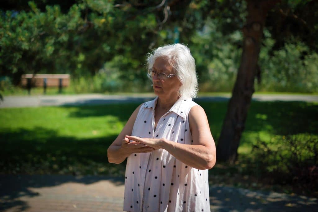A woman stands in a park with her hands together.
