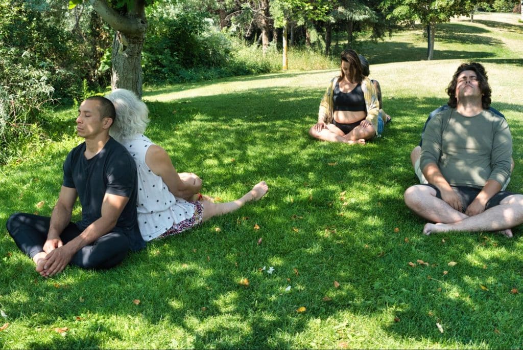 A group of people sit in pairs on the grass back to back.