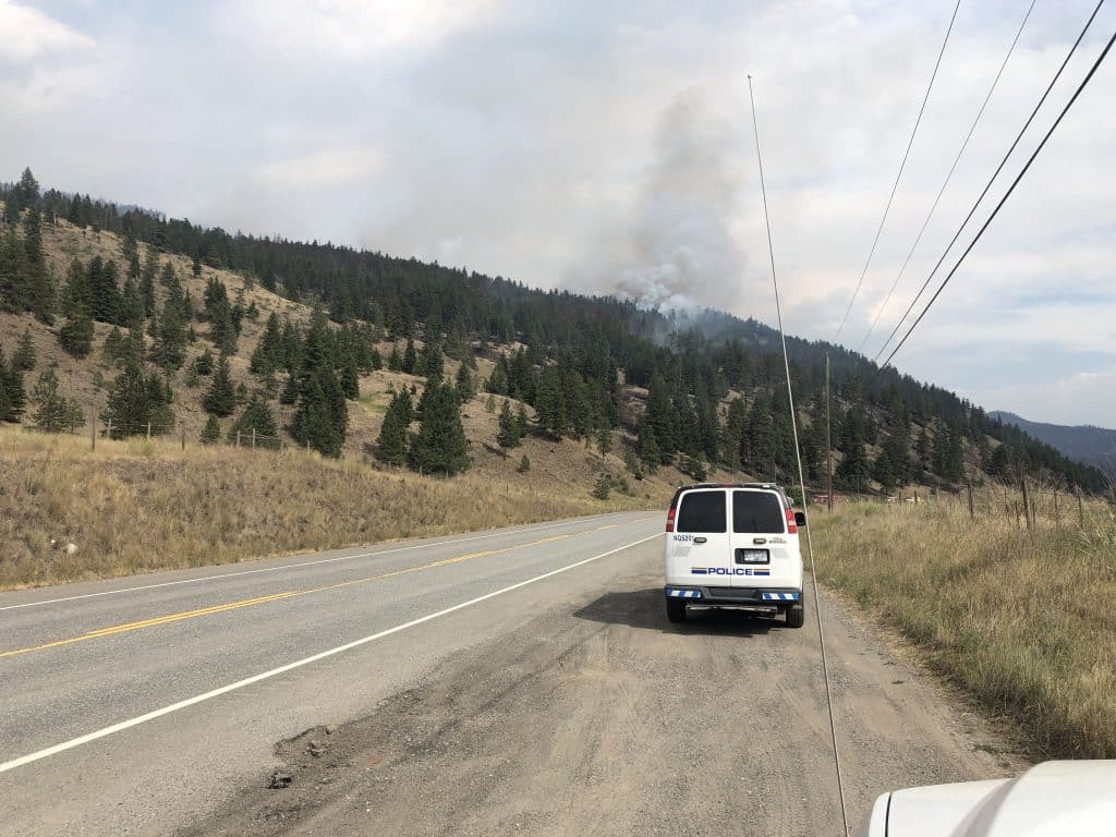A white van drives toward smoke behind a mountain slope