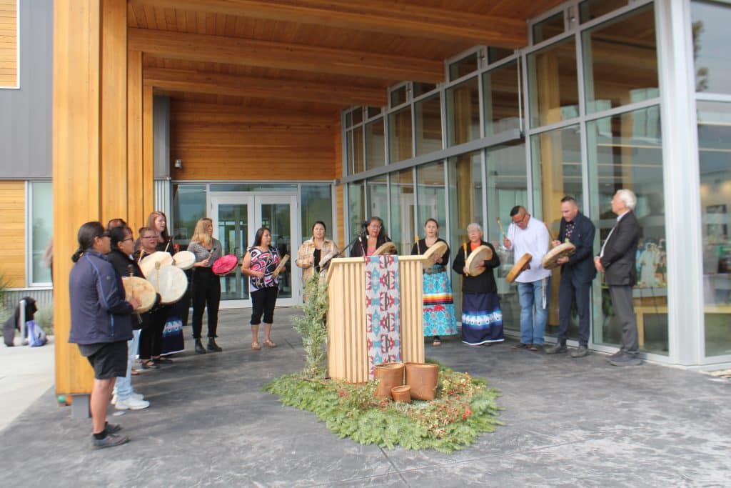 A group of leaders stand in front of a podium with a mic, a few hold drums as they sing.