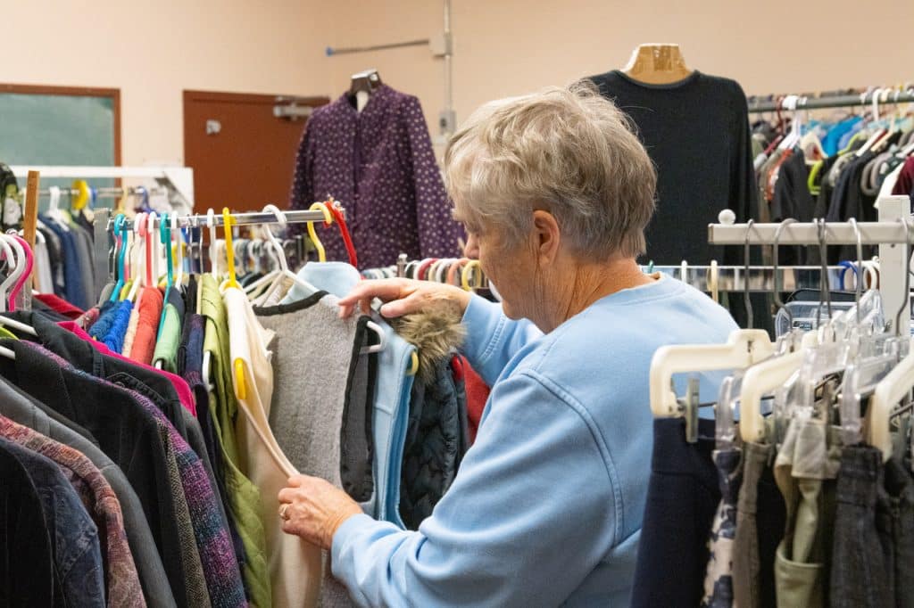 A woman in blue sorts through clothes at a thrift shop. 