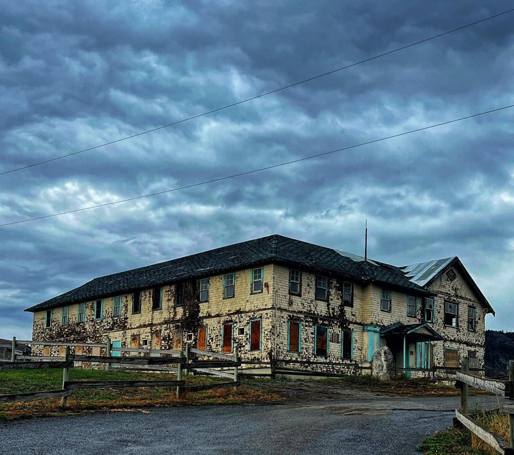 An old sanatorium building stands decrepit amidst moody dark skies.