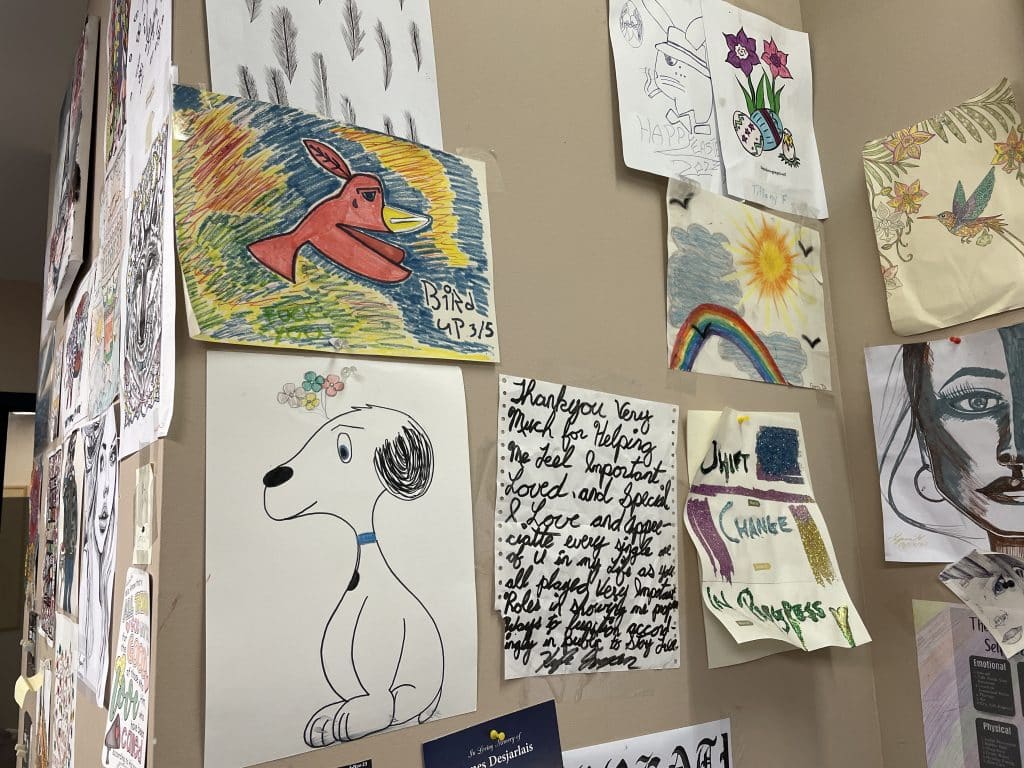 Drawings are posted on the wall at Merit Place. Next to a drawing of a dog, a handwritten letter reads: "Thank you very much for helping me feel important, loved and special. I love and appreciate every single one of u in my life as you all played very important roles in showing me purpose and ways to function accordingly in public to stay well."