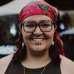 Photo of Shay Paul wearing a red bandana and large framed glasses, smiling.