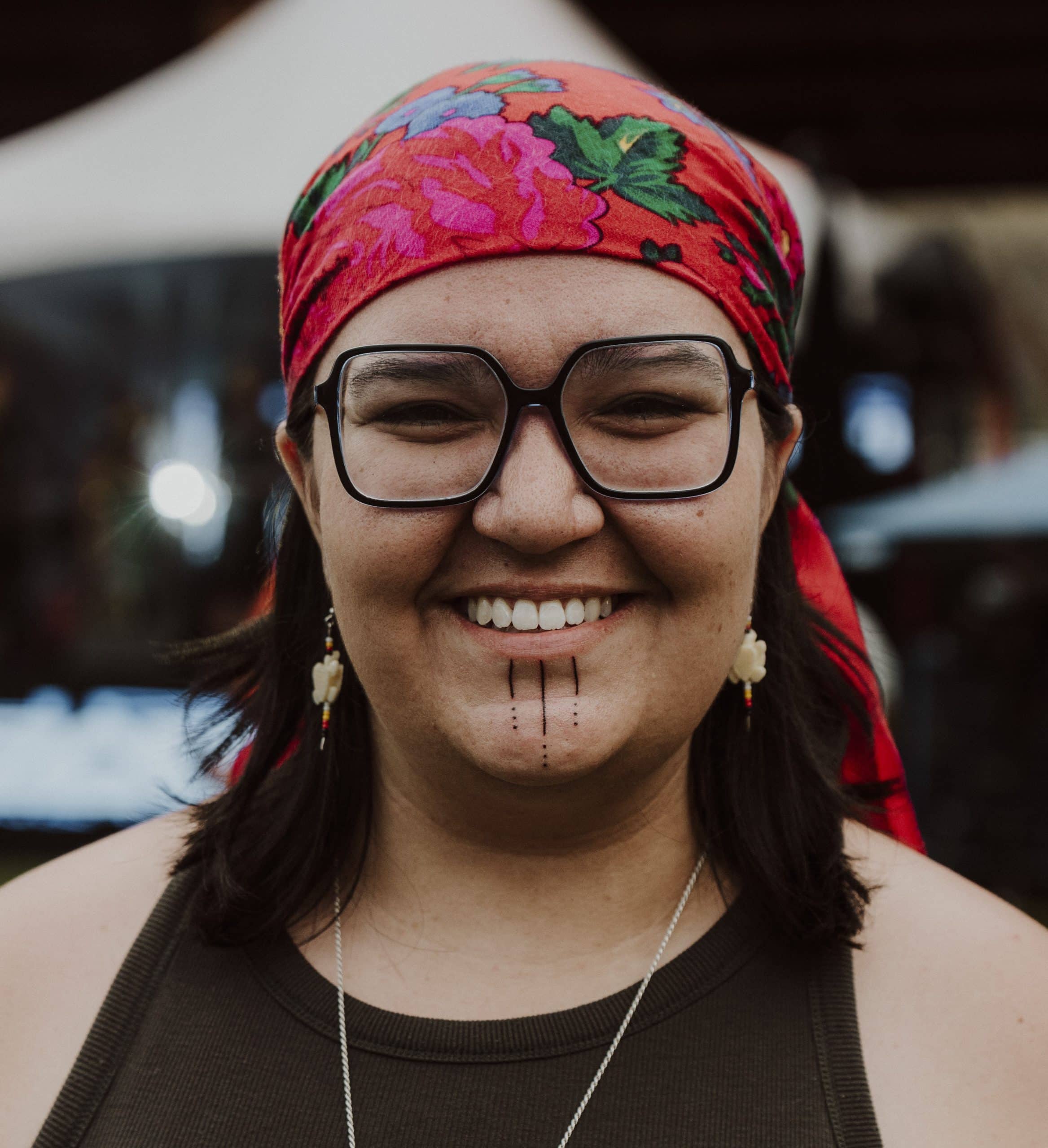 Photo of Shay Paul wearing a red bandana and large framed glasses, smiling.