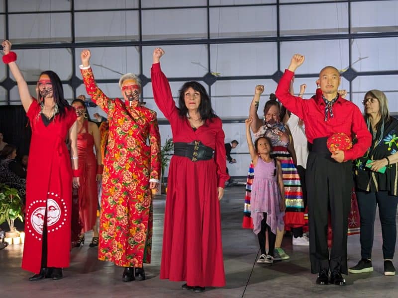 Several people wearing red stand in the center of the photo. They all have their right hand raised and their fist clenched.