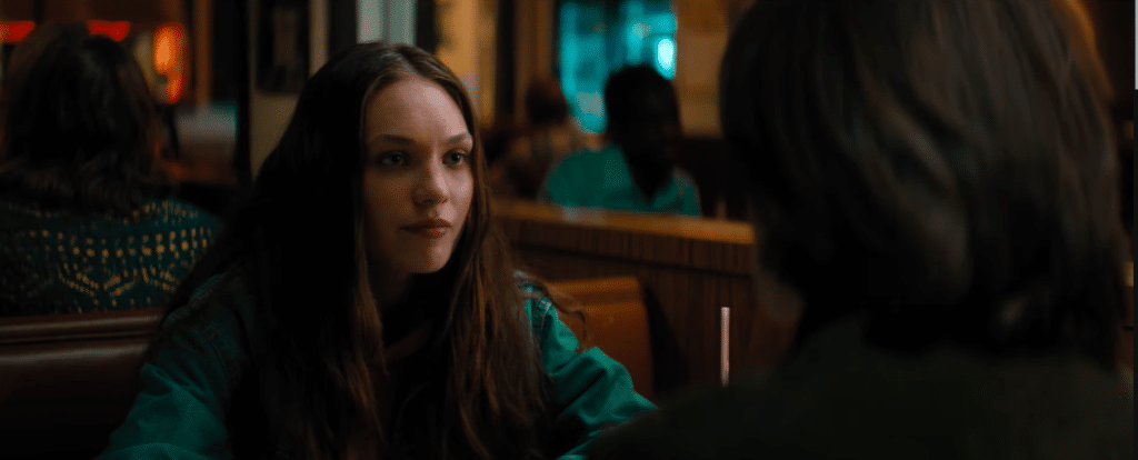 Photo shows two people sitting in a dinner. The person on the right is facing away and you cannot see their face at all. The person on the left is a young teenage girl with long hair.