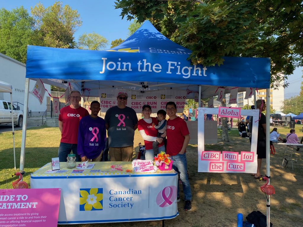 Volunteers of the CIBC Run for the cure under a tent smiling.