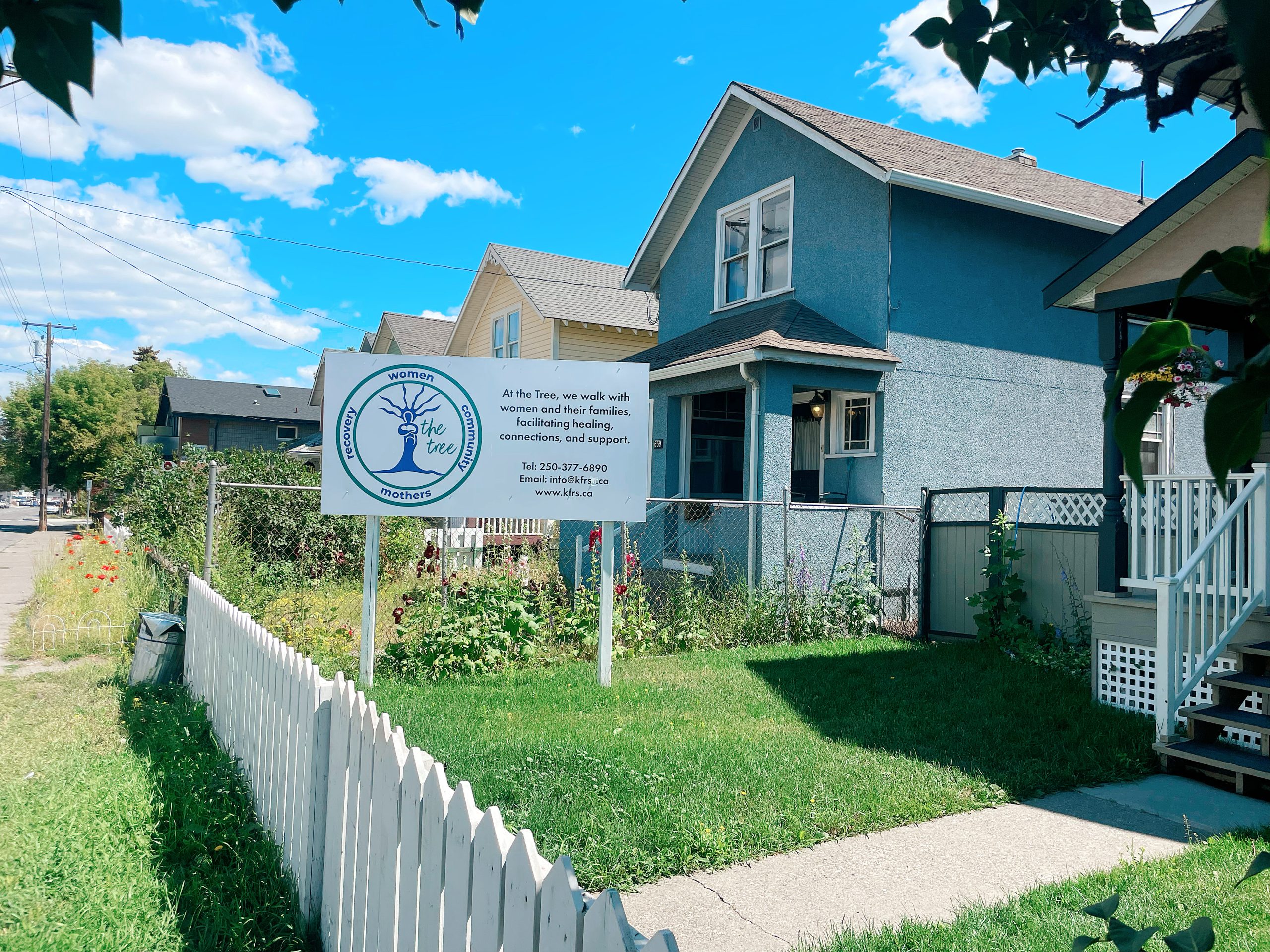 A blue house is shown with a picket fence and a sign that reads The Tree in front of a green lawn