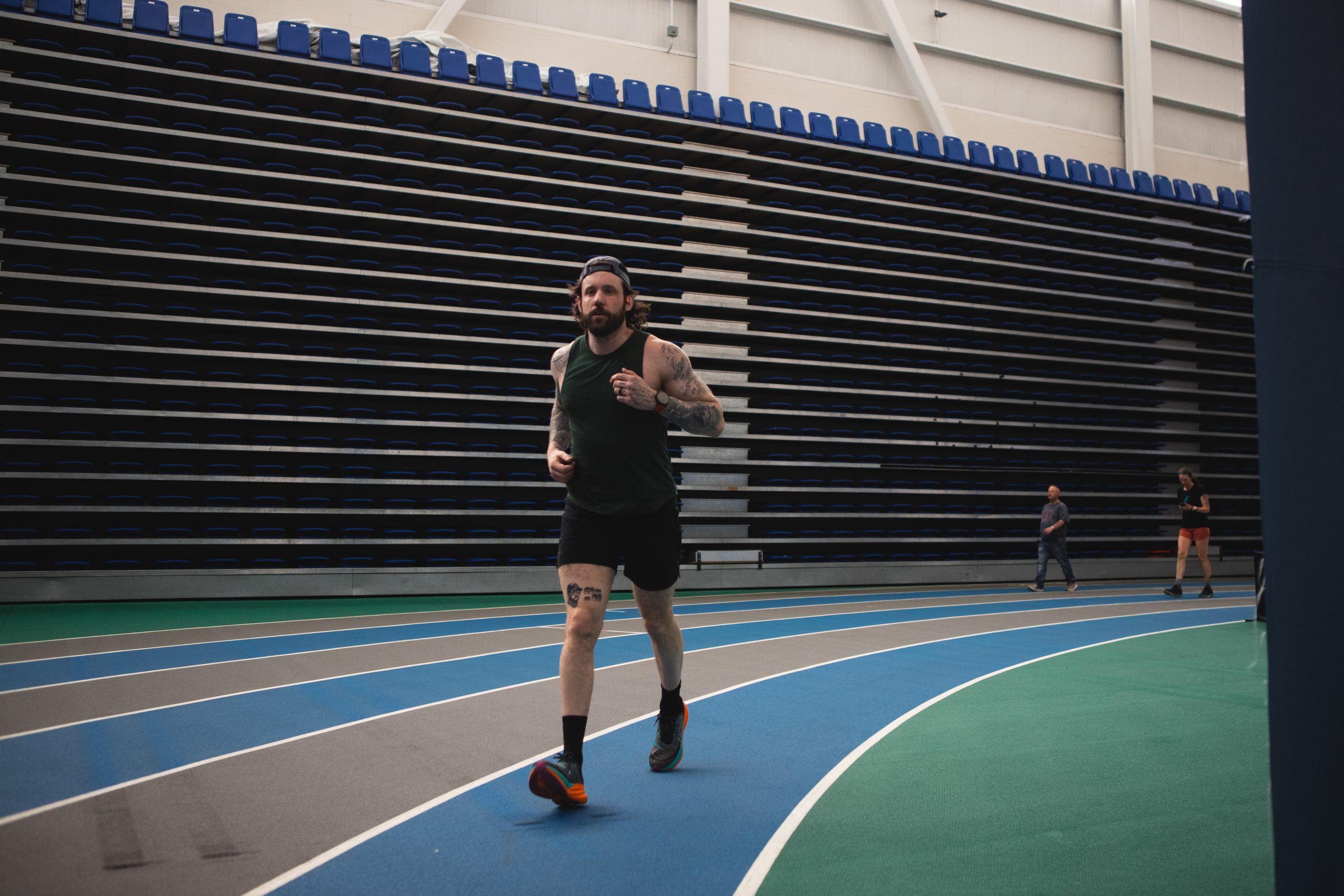 A man is seen running in the indoor track, the track has 6 paths each of them has alternating colors of grey and blue. The man is running on a blue track