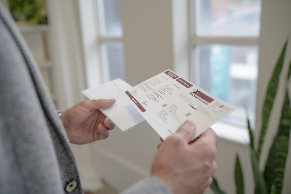 The voter information card is in the hands of a person. Candidates answer questions on homelessness and housing disparities. 