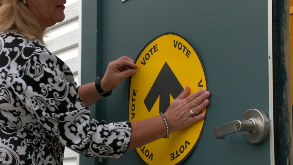 A woman is putting up a vote sign on one of the polling stations. Candidates answer questions on affordability.